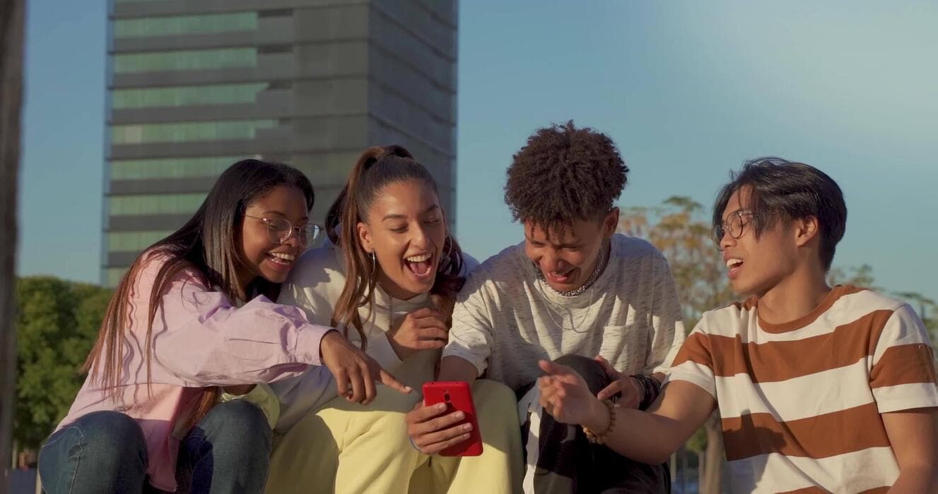Four teens laughing together while looking at a phone